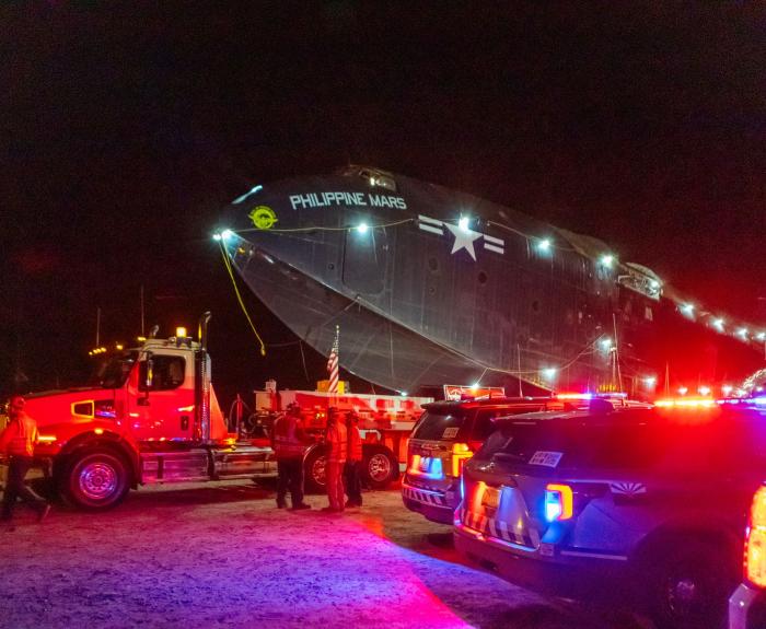 Photo of the seaplane loaded on the back of a large truck and trailer. 