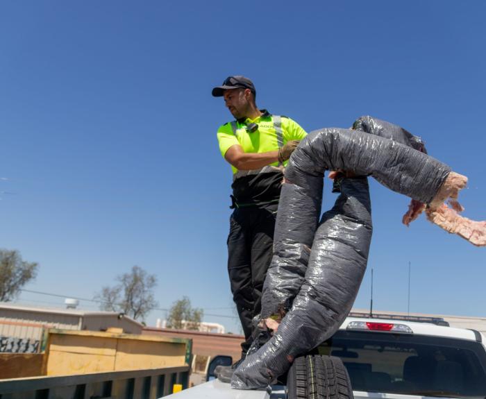 An ADOT employee tossing debris from the highway in to the dumpster.