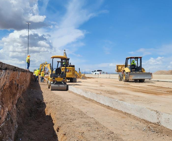 Heavy equipment operates in a highway work zone in Arizona as a man stands nearby.