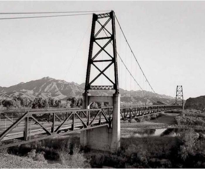 A black and white photo of a rural bridge over a river.