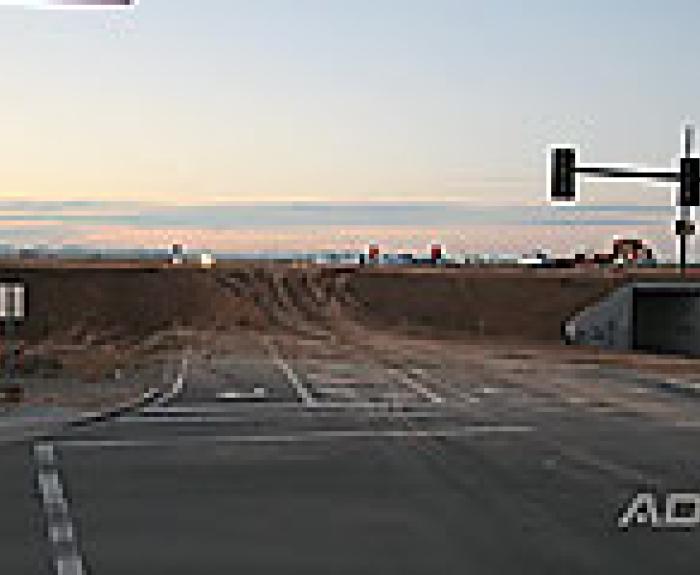 A paved road ends abruptly at a dirt embankment under construction, with traffic lights and an underpass visible on the right side.