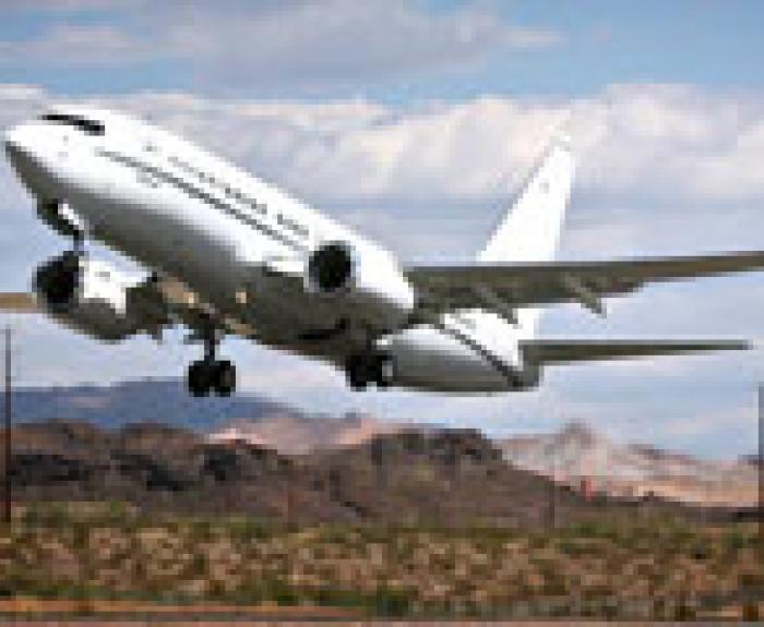 A white commercial airplane taking off from a runway with mountains and desert landscape in the background.