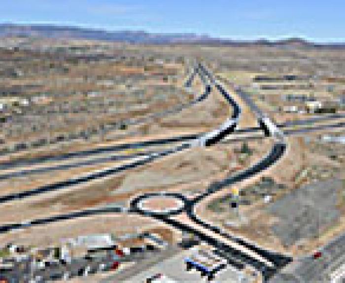 Aerial view of a highway interchange with multiple lanes, a roundabout, overpasses, and surrounding dry, open landscape.