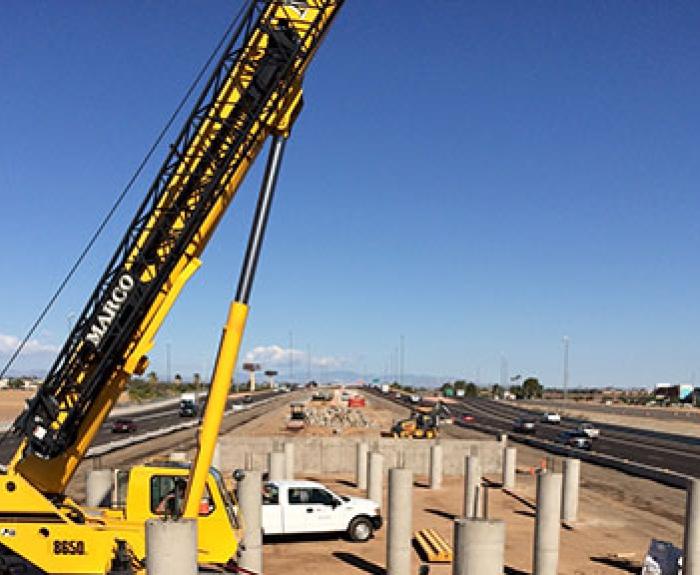 A yellow crane and concrete pillars at a highway construction site under a clear blue sky.