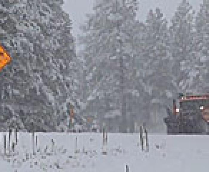 Snow plow on a snowy road with watch for ice sign