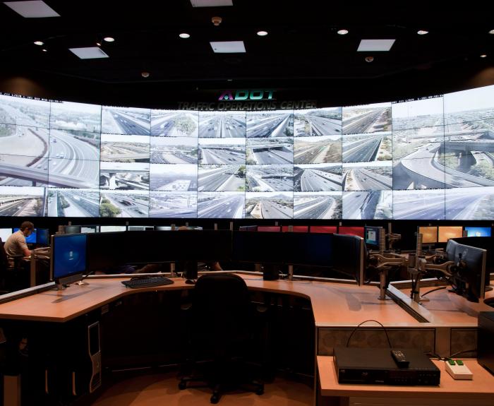 A traffic operations center with large screens displaying live highway camera feeds and empty workstations.