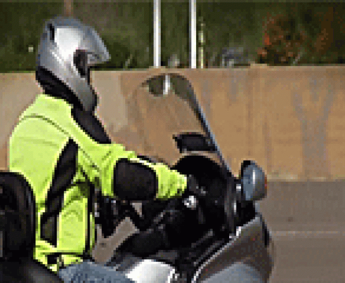 A motorcyclist in a neon yellow jacket and helmet rides a motorcycle.