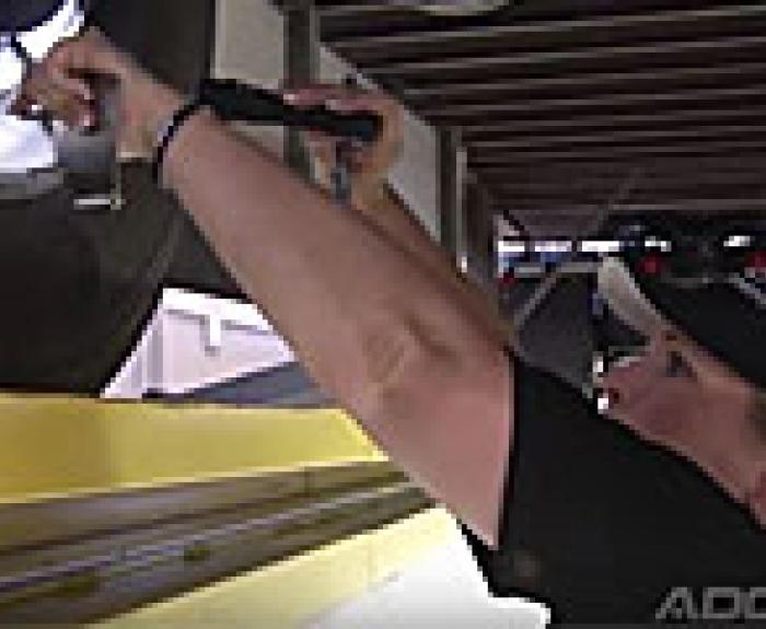 Person inspecting or repairing a large vehicle wheel with a tool underneath a structure.