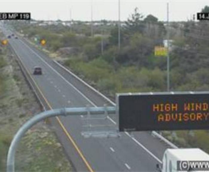 High wind advisory sign above a mostly empty highway with cars in the distance.