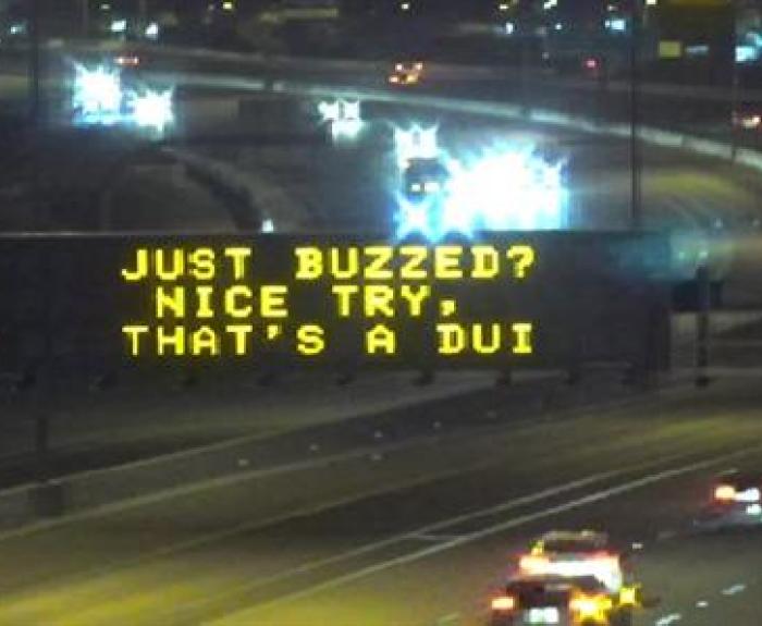 Highway sign at night reads: Just buzzed? Nice try, thats a DUI. Cars are visible on the road.