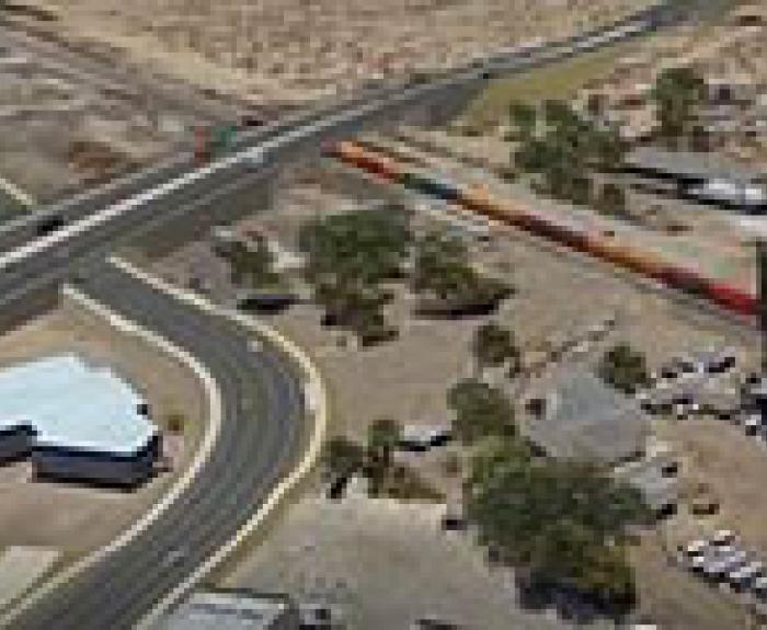 Aerial view of a highway overpass crossing above a railroad track with a train, surrounded by roads, buildings, and a water tower in a desert area.