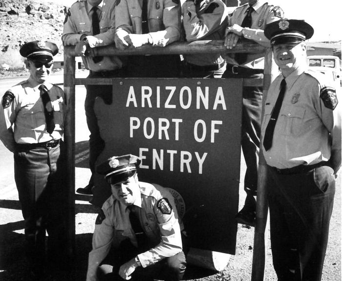 Black and white photo of seven MVD enforcement officers standing with Arizona port of entry sign