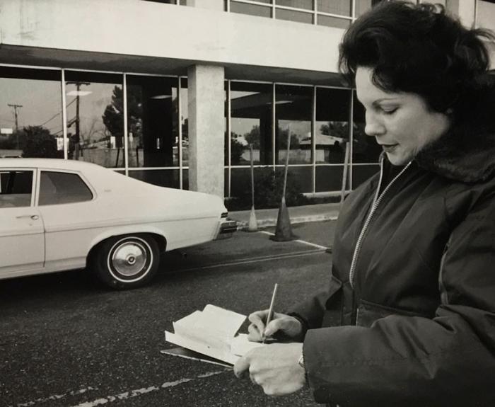 Black and white photo of road test reviewer writing on notepad in front of car