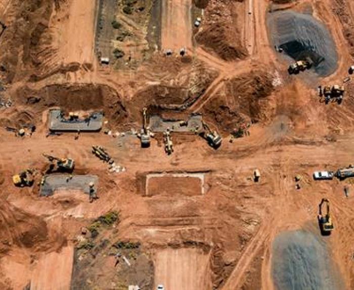 Aerial view of a large construction site with machinery, trucks, and dirt roads on reddish soil.