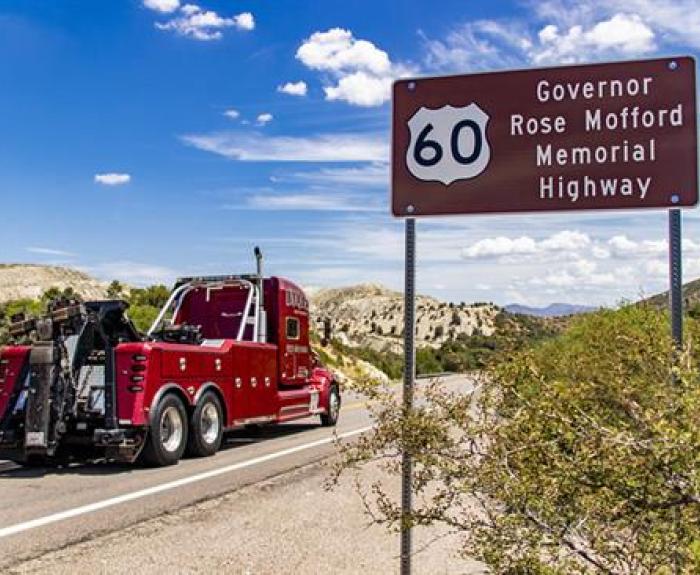 A red tow truck drives on a highway near a sign for Governor Rose Mofford Memorial Highway US 60.