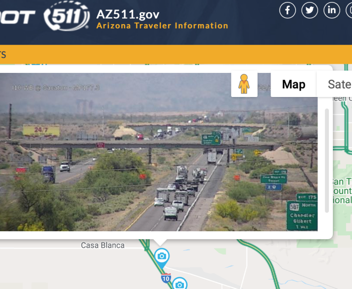 Traffic camera view of a busy highway in Arizona with cars, trucks, and desert landscape in the background.