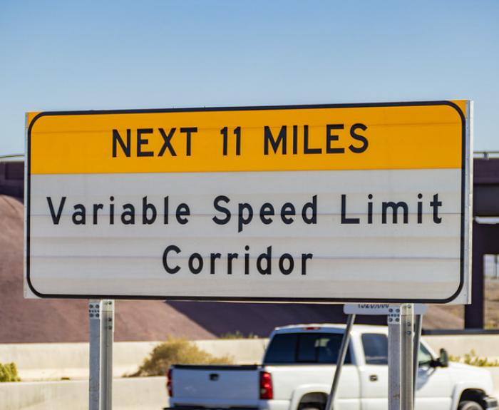 Road sign reads: Next 11 miles, Variable Speed Limit Corridor, with a white truck in the background.