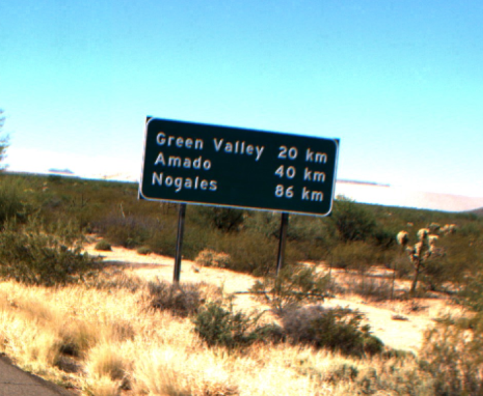A road sign in a desert landscape shows distances to Green Valley (20 km), Amado (40 km), and Nogales (86 km).