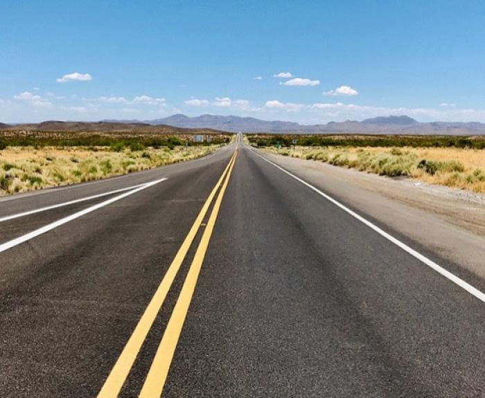A straight empty Northern Arizona highway stretches into the distance under a clear blue sky with mountains ahead.