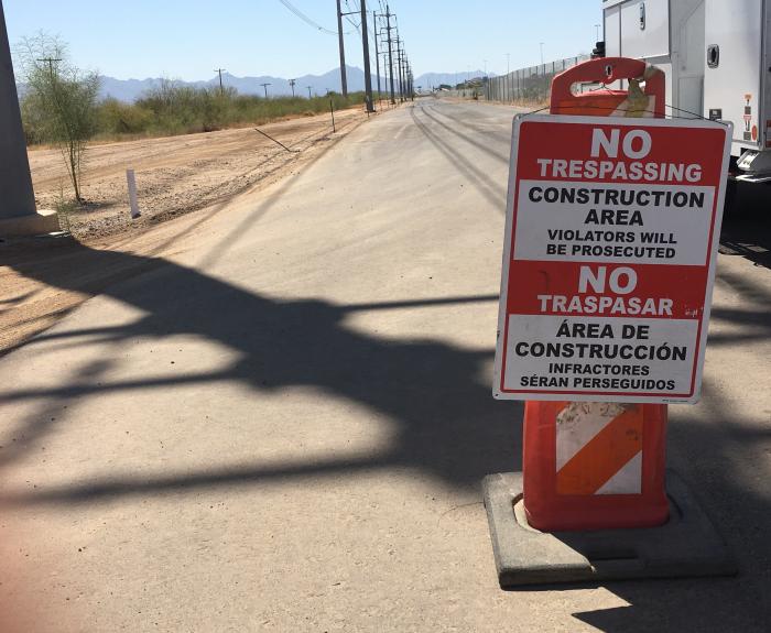Orange barrier with a bilingual No Trespassing, Construction Area warning sign on a paved road.