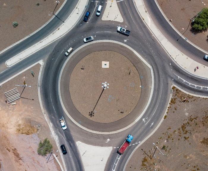Aerial view of a roundabout with multiple cars driving, surrounded by desert landscape and sparse vegetation.