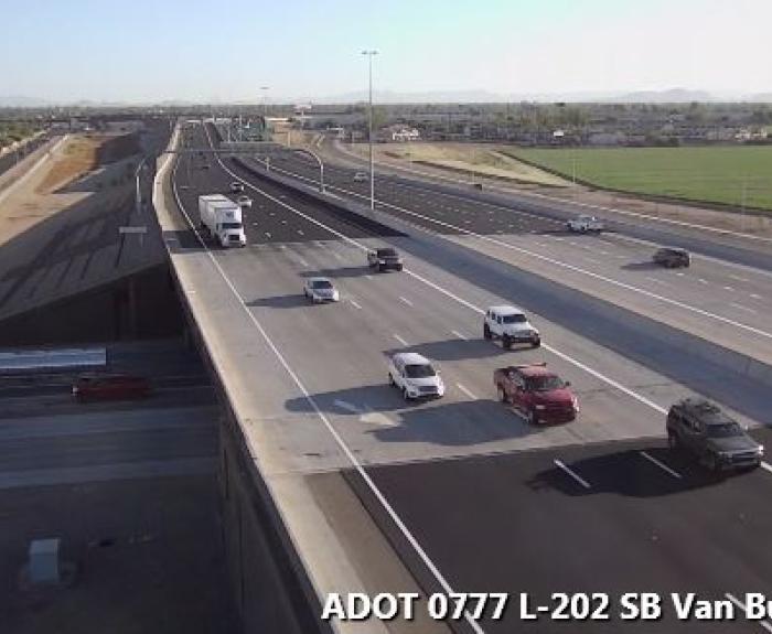 Several cars and trucks drive on a wide highway overpass near fields, under a clear sky.
