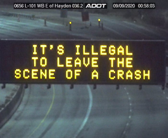 Electronic highway sign displays the message ITS ILLEGAL TO LEAVE THE SCENE OF A CRASH on an empty roadway at night.