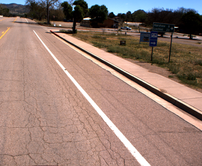 A road with a sidewalk and a sign showing directions to Harshaw and Lochiel under a clear sky.