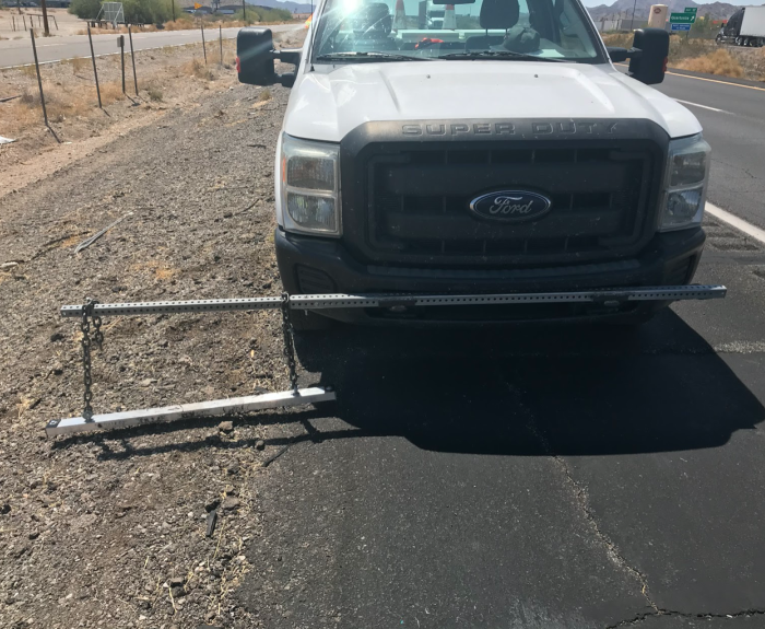 A white Ford Super Duty truck with a pickup bar mounted on its front bumper by the roadside.