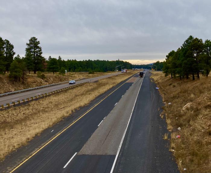 A divided highway with a few cars, bordered by trees and dry grass under a cloudy sky.