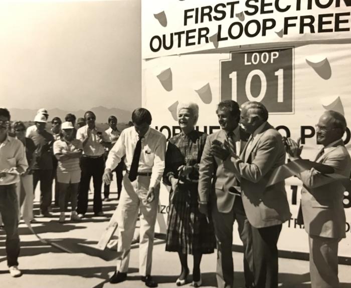 Black and white image of people in front of large Loop 101 grand opening sign