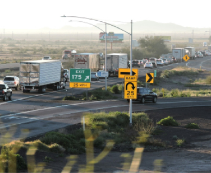 Cars and trucks are lined up in slow-moving traffic on a highway near an exit, with road signs indicating a 25 mph speed limit and a U-turn.