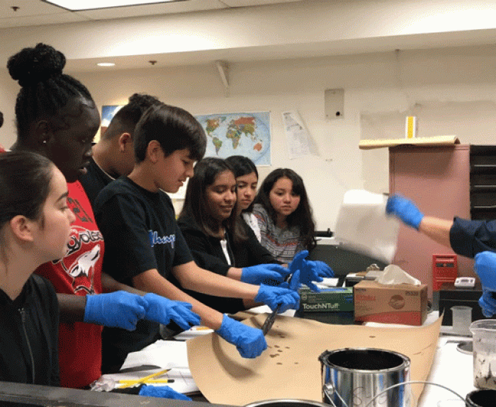 Students watch ADOT workers test materials on a table.