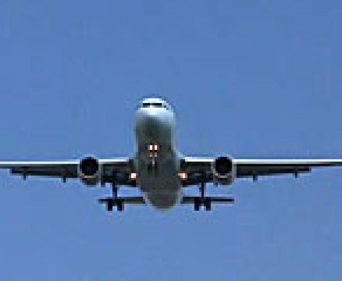 A commercial airplane is flying in a clear blue sky, viewed from below with its landing gear extended and wings level.