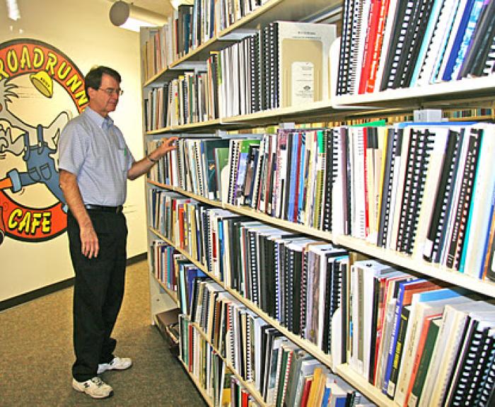 Man browsing binders on a library shelf near a wall with a Roadrunner Café cartoon mural.