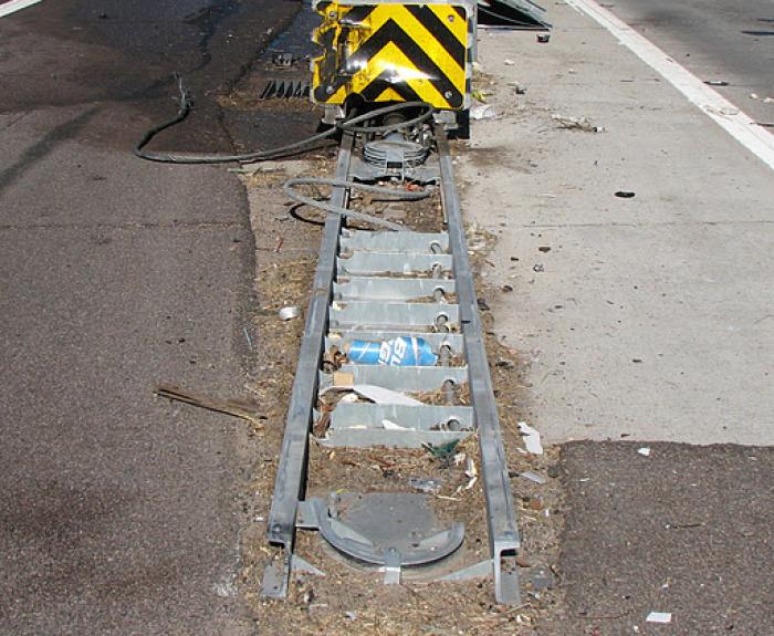 Damaged crash barrier with black and yellow stripes on a roadside, metal parts bent and debris scattered.