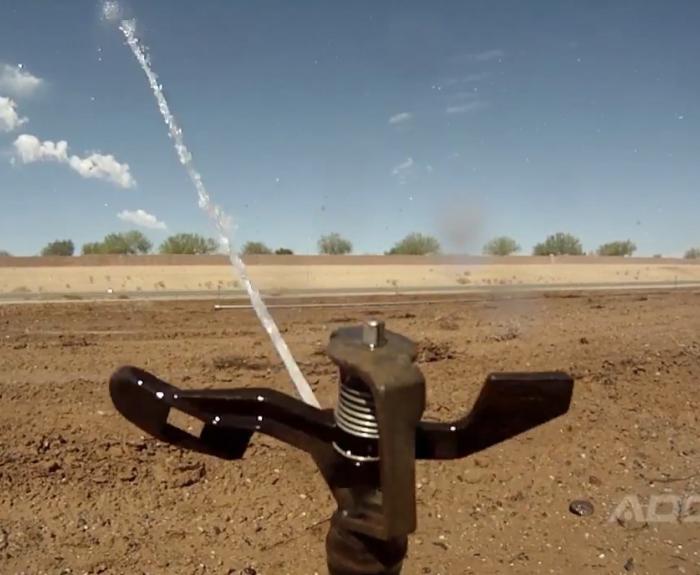 Sprinkler wets earth at highway construction site. 