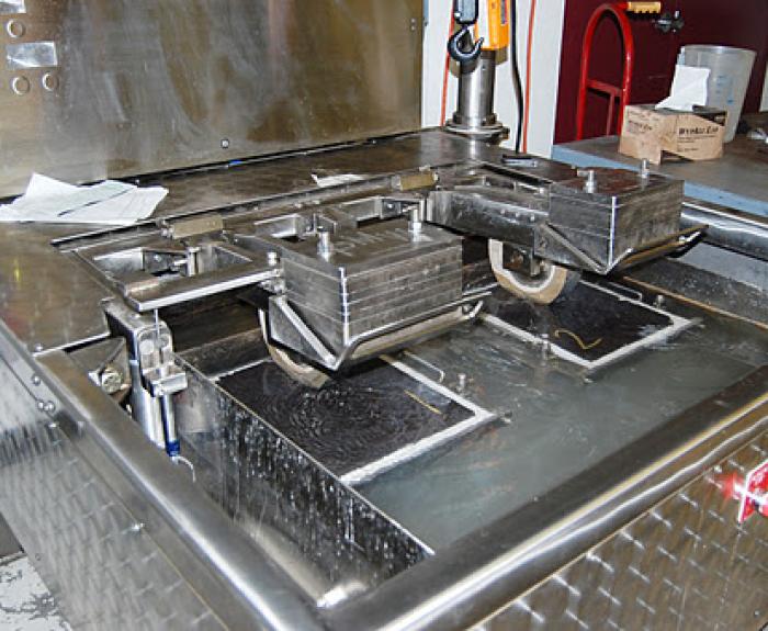 A large industrial machine with metal trays and rollers used for testing asphalt and other road materials.