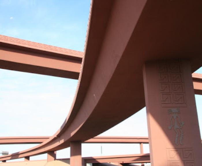 Brown freeway overpasses with geometric patterns against a blue sky, viewed from below.