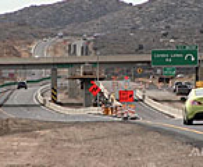 Cars drive on a divided highway near a construction zone with orange warning signs, cones, and an exit sign for Cordes Lakes, surrounded by hills.