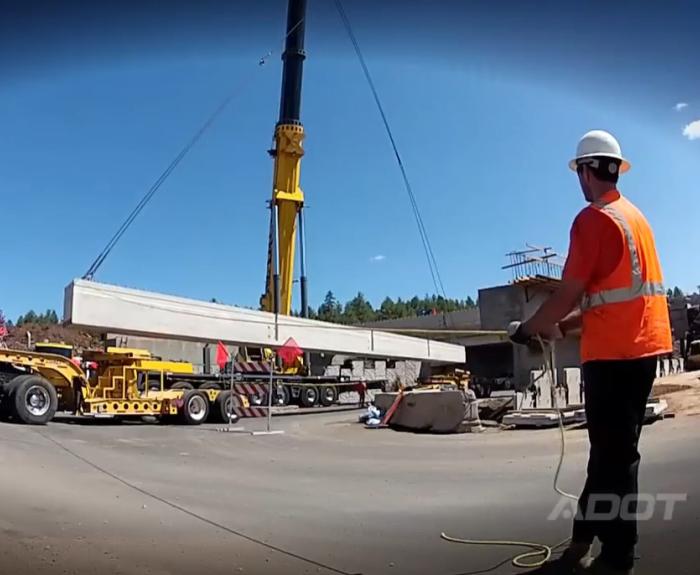 Crane lifts box girder from truck trailer.