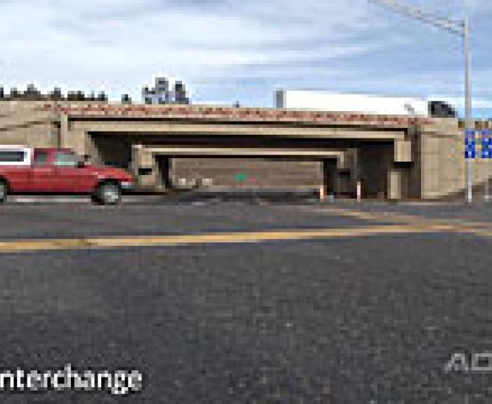Red SUV and white truck drive near a new highway interchange under an overpass, with road signs visible.