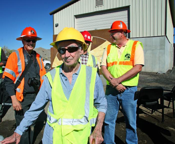 Four people in hard hats and safety vests, one of whom is architect Paolo Soleri, stand outside an industrial building.