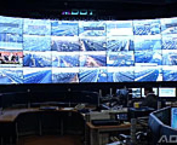 A control room with many monitors displaying live traffic camera feeds on a large curved wall screen.