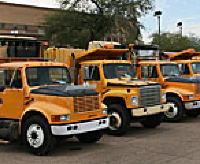 Four yellow dump trucks are parked in a row on a paved lot.