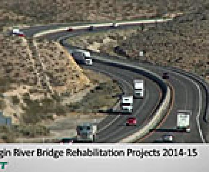 A highway with multiple lanes curves through a desert landscape, carrying several cars and trucks. Text reads: I-15 Virgin River Bridge Rehabilitation Projects 2014-15.