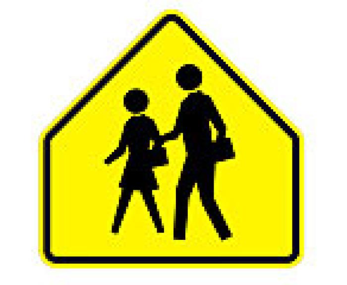 Yellow pentagon traffic sign with silhouettes of an adult and a child walking, indicating a school zone or pedestrian crossing ahead.