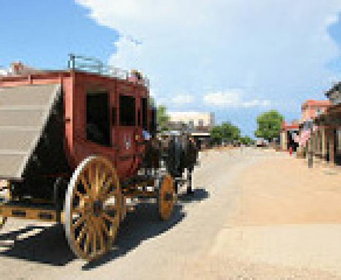 A horse-drawn stagecoach travels down a deserted, sunlit street in the historic town of Tombstone Arizona with wooden buildings on either side.