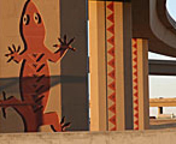 Large red lizard artwork painted on concrete support pillar under a highway overpass, with geometric patterns on adjacent pillars and highway in background.