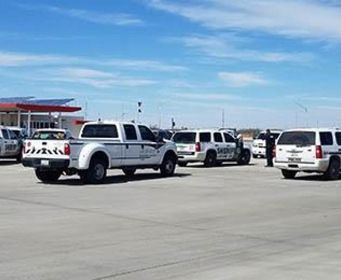 Multiple emergency response vehicles are parked in a large open lot under a blue sky with scattered clouds.